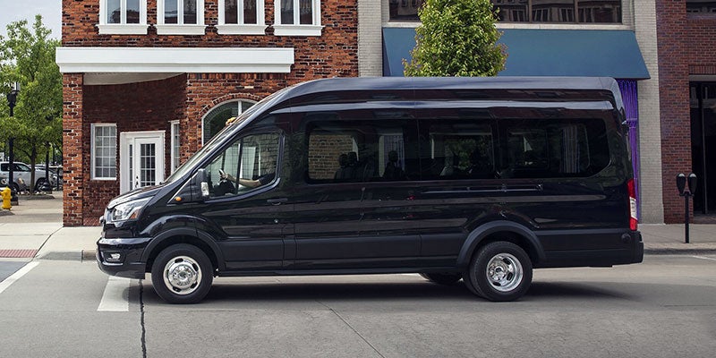 Black passenger van parked on a city street in front of a brick building.