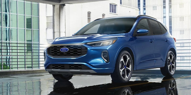 Blue Ford Escape SUV parked at an angle on a wet asphalt surface, with buildings in the background.