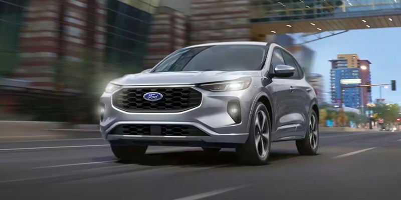 Silver Ford Escape SUV driving on a city street with headlights on.