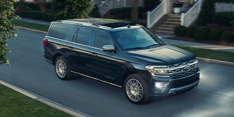 Black Ford Expedition SUV with a sunroof driving on a paved street past houses.