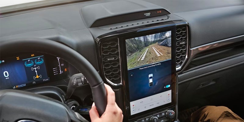 Car interior with a hand on the steering wheel, a large screen displaying an off-road camera view, and a digital dashboard.
