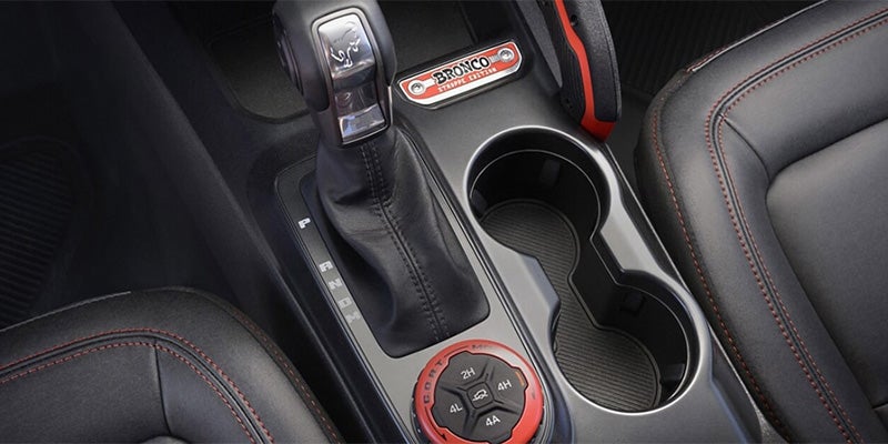 Car interior with automatic gear shifter, cup holders, 4x4 drive mode dial, and a 'Bronco Sport Edition' badge.