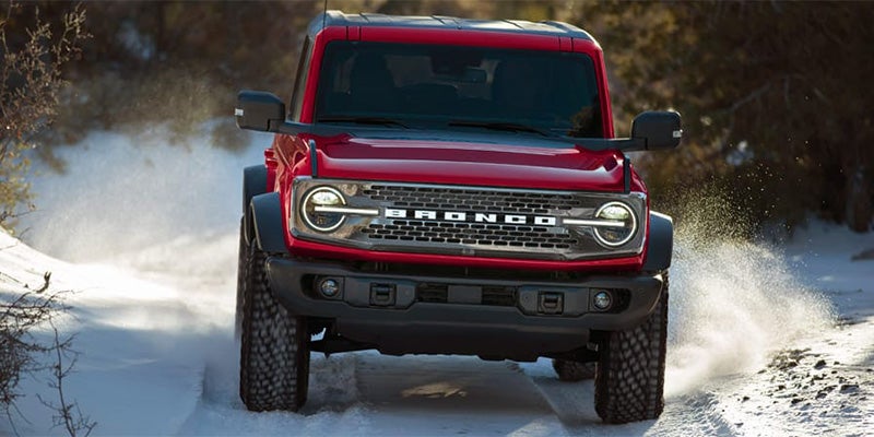 Red Ford Bronco SUV driving through deep snow, kicking up powder from its tires.