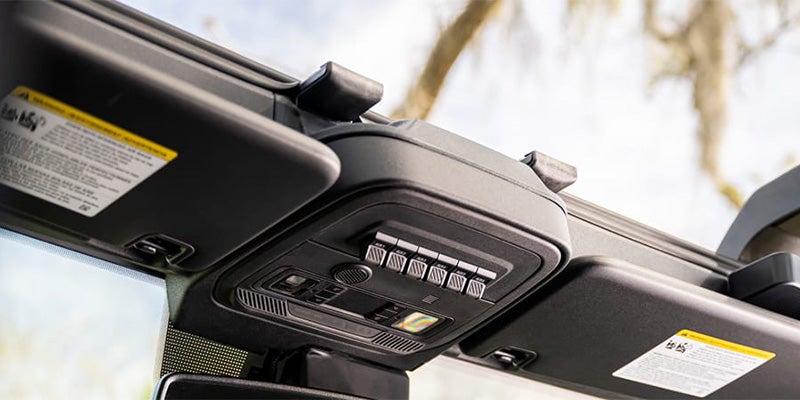 Overhead console of a vehicle with auxiliary switches, interior lights, and sun visors with warning labels.