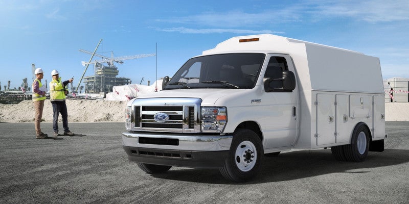 White Ford E350 utility truck at a construction site with two workers discussing plans in the background.