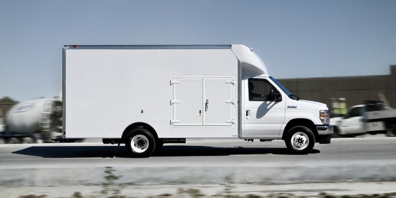 White utility box truck with side compartments driving on a road, with motion blur.