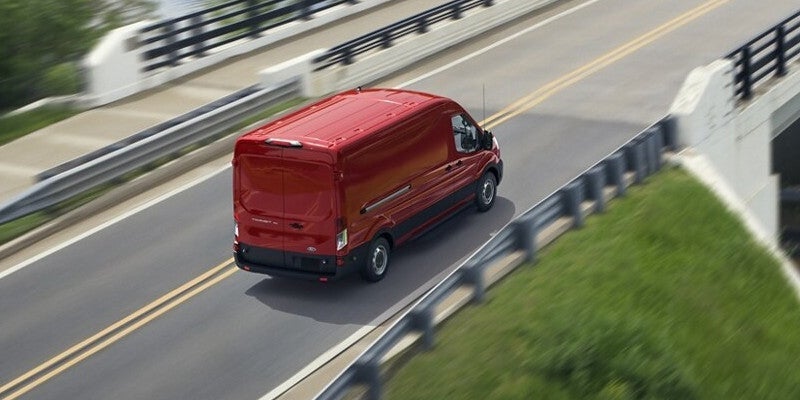 Red cargo van driving on a highway overpass, viewed from above, with motion blur indicating speed.