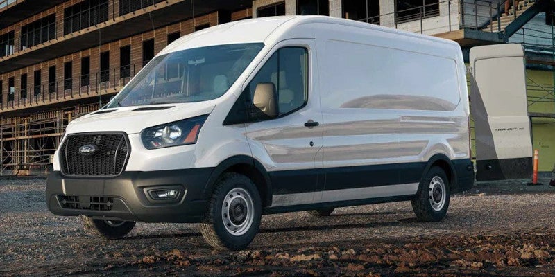 White Ford Transit cargo van parked on a dirt lot in front of a building under construction.