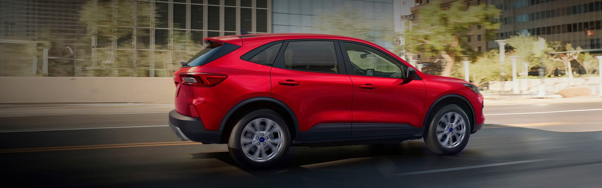 Red Ford Escape SUV driving on a road with blurred urban background, conveying motion.