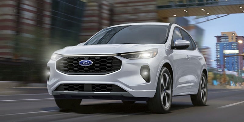 White Ford Escape SUV driving on a city street with motion blur, headlights on.
