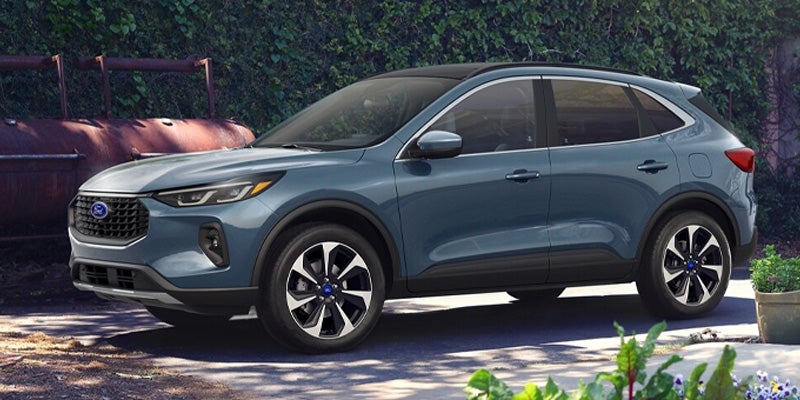 Slate blue Ford Escape SUV parked outdoors with two-tone wheels, a black roof, and green foliage in the background.