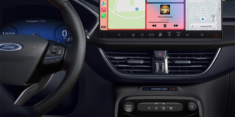 Car interior with a steering wheel, digital dash, and an infotainment screen showing navigation and music.
