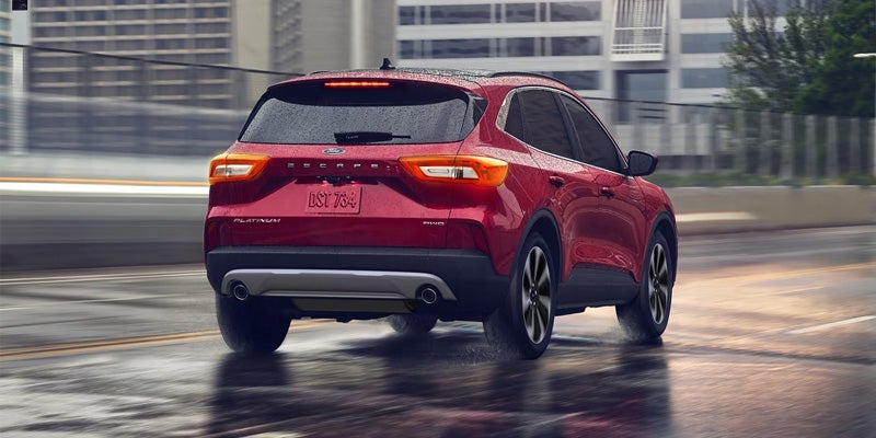 Red Ford Escape SUV driving away on a wet city road, rear and side visible