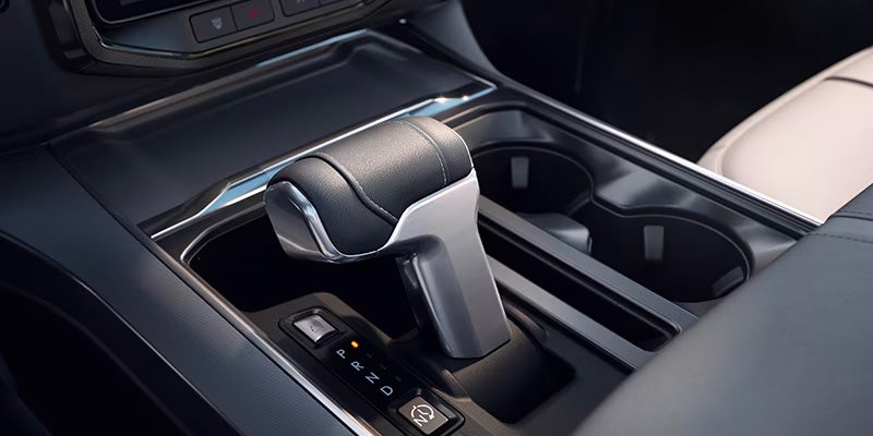 Modern car interior showing a sleek gear shifter, with the gear selector illuminated at "P" (Park), and cupholders.