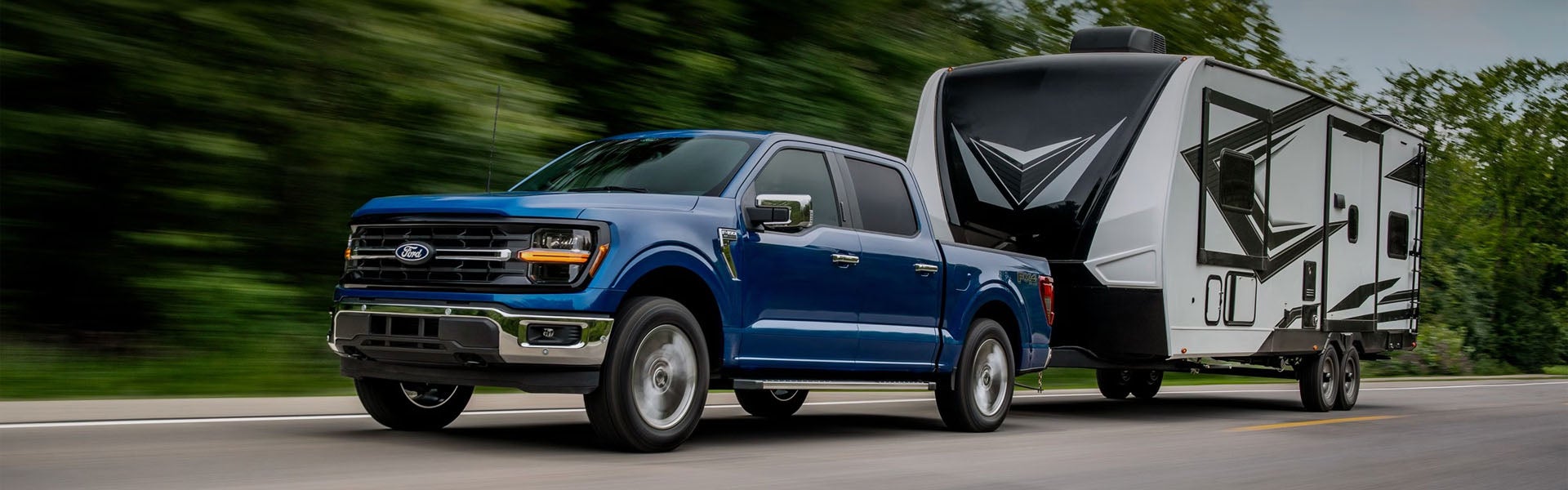 A blue Ford pickup truck pulls a white and black travel trailer down a road