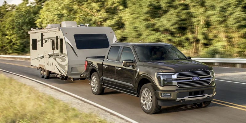 Dark pickup truck towing a light-colored travel trailer on a road
