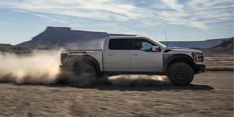 White Ford Raptor truck kicking up dust while driving through a desert landscape