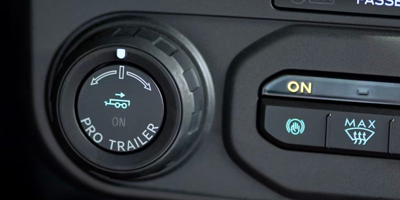 Car interior showing a "PRO TRAILER" control knob with a trailer icon, next to an illuminated "ON" button.