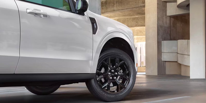 White SUV front driver's side with a black multi-spoke wheel, parked in a concrete garage.