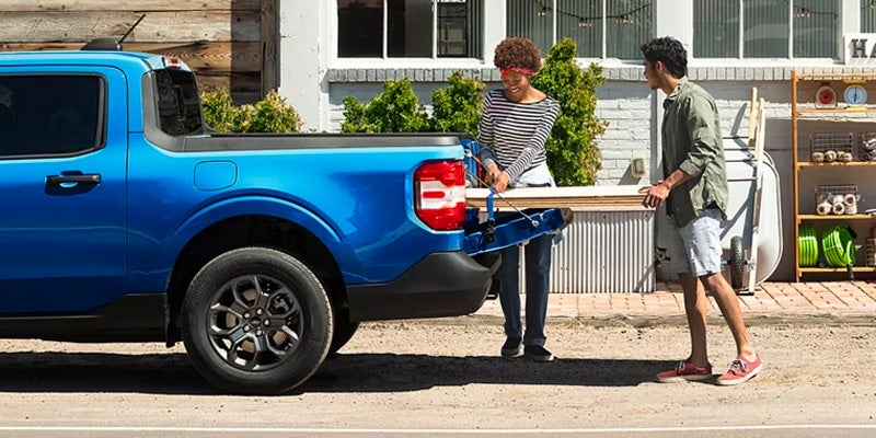 A couple loads lumber into the bed of a blue pickup truck with its tailgate open.