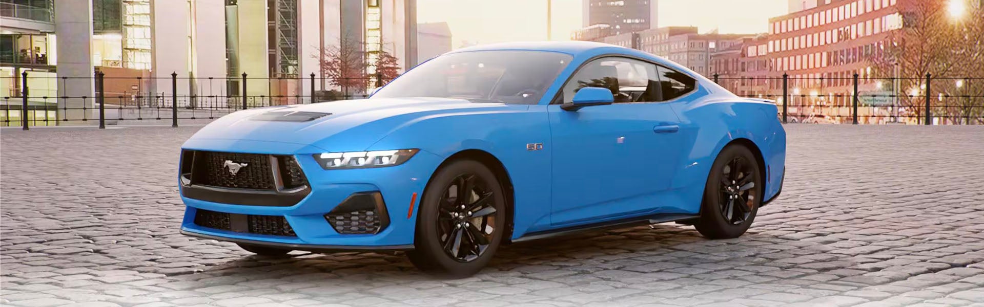 A blue 2024 Ford Mustang sports car parked on a cobblestone street in a city.