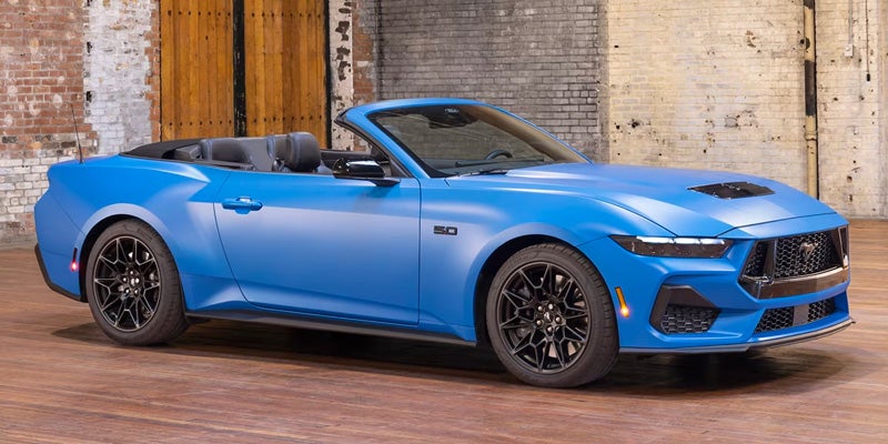 Blue convertible Ford Mustang with its top down, parked in a studio with brick walls.