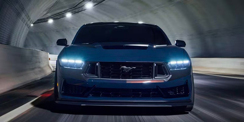 Dark blue Ford Mustang driving head-on in a tunnel, its bright headlights illuminating the way.