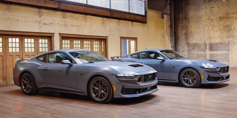 Two grey Ford Mustang sports cars with black accents parked indoors, angled to show the front and side profiles.