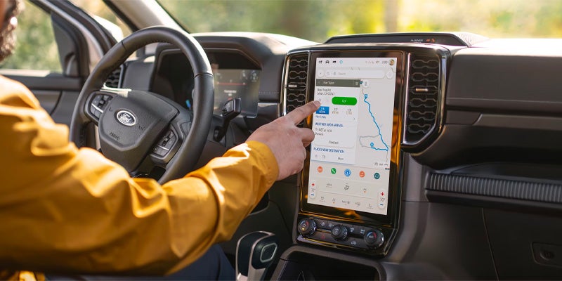 A person's hand touches a large vertical infotainment screen showing a navigation map inside a Ford car.