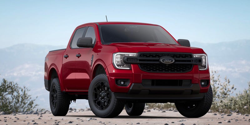 Red Ford Ranger pickup truck with black grille and wheels, parked on a rocky trail with mountains in the background.