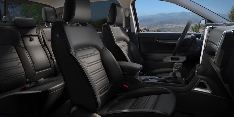 Car interior with black leather seats and a view of mountains through the window.