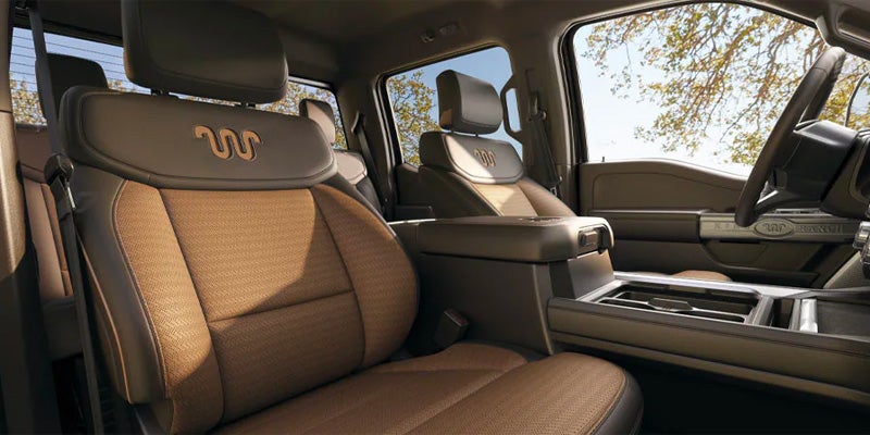 King Ranch truck interior with brown and black leather seats, embroidered logos, center console, and view of trees outside.