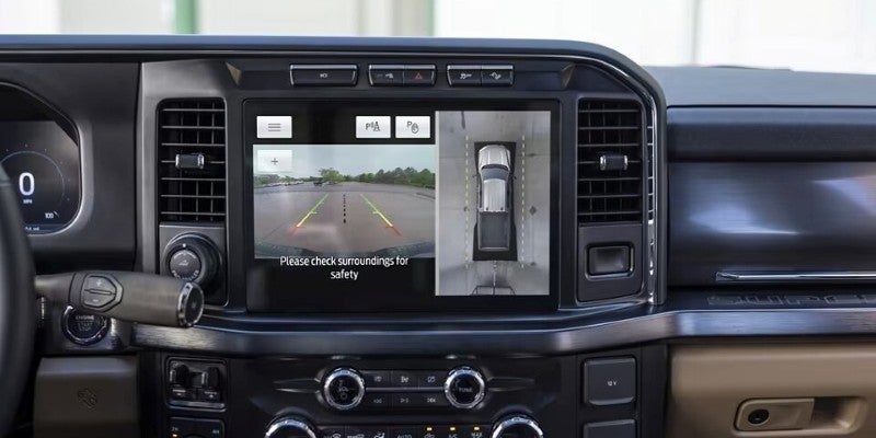 Car infotainment screen showing split view: rear backup camera with guidelines and overhead 360-degree truck view.