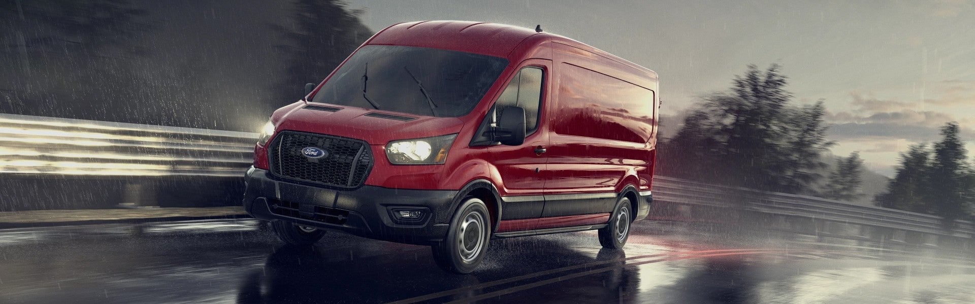Red Ford Transit van driving on a wet road in the rain, headlights on