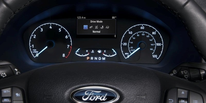 A car's illuminated dashboard showing the speedometer, tachometer, and a digital display set to "Normal" drive mode.