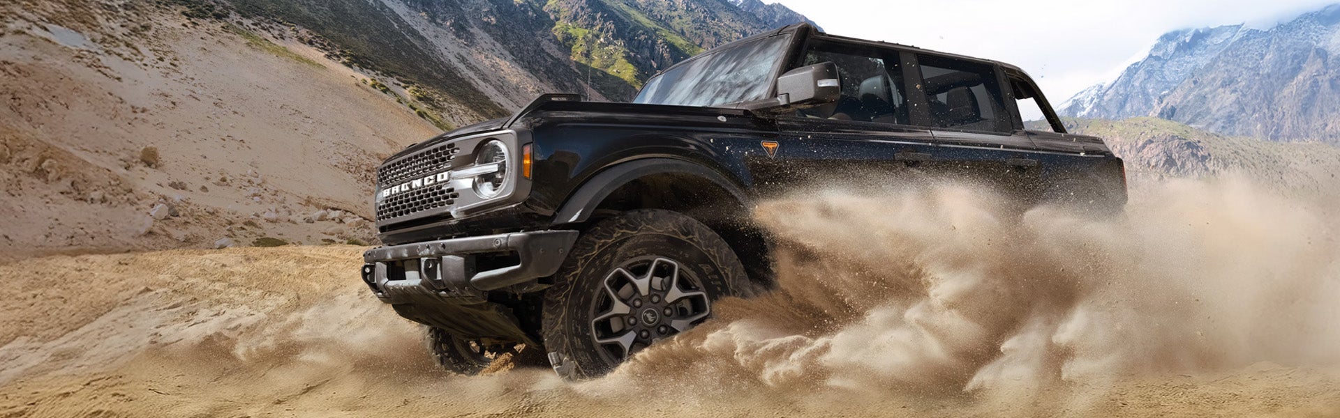 Black Ford Bronco kicking up a huge cloud of dust while off-roading in a dry, mountainous landscape.