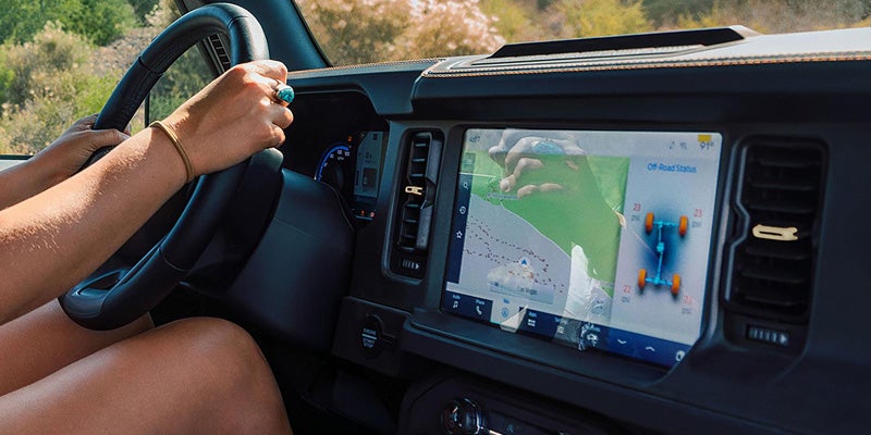 Hands on a steering wheel inside a vehicle with an infotainment screen displaying a map and off-road tire pressure.