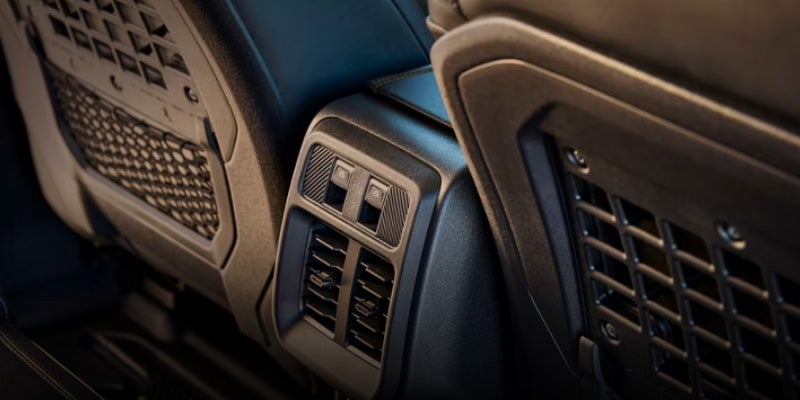 Rear passenger console with air vents, USB ports, and storage pockets on dark car seatbacks.