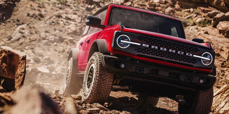 Red Ford Bronco 4x4 driving over rocky terrain.