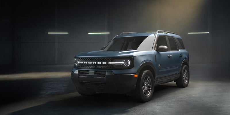 A teal Ford Bronco Sport SUV with a black grille and round headlights is parked indoors, angled slightly to the right.