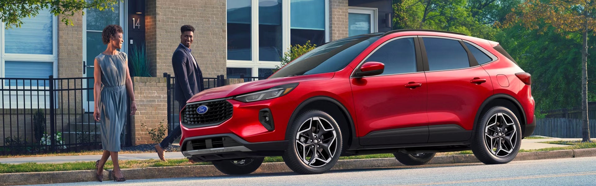 Red Ford SUV parked on a suburban street as a man and woman walk by, smiling.