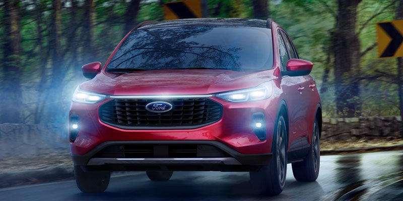 Red Ford SUV with bright headlights on, driving toward the viewer on a wet road surrounded by blurred trees.