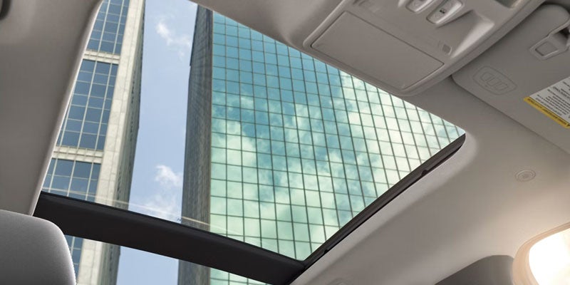 View from a car's sunroof looking up at tall city buildings with reflective glass facades.