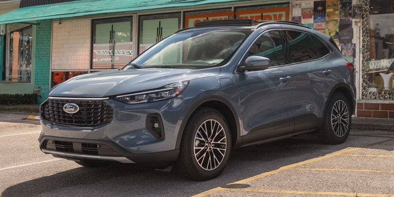 A gray Ford Escape SUV parked on asphalt in front of a storefront with reflections in the windows.