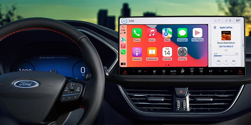 Car interior with a Ford steering wheel and a large infotainment screen displaying Apple CarPlay apps like Music, Maps, and Phone.