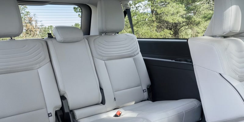 Light gray leather car interior with second and third-row seats, seen from the side, with trees visible outside the windows.