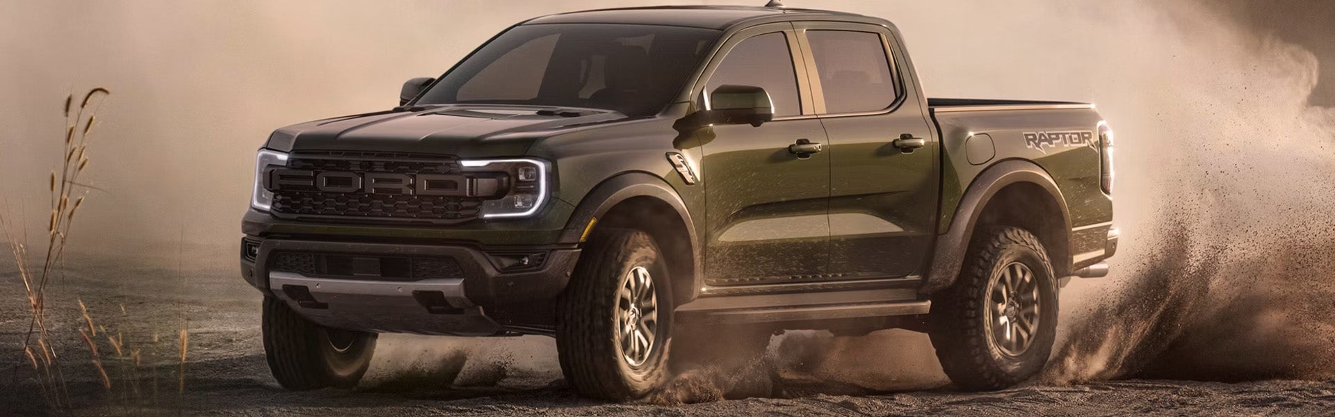 Dark green Ford Ranger Raptor pickup truck kicking up dust while driving off-road.