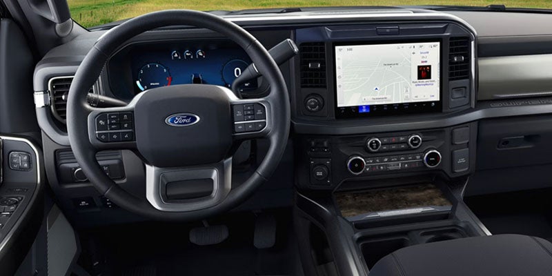 The interior of a Ford F-150 with a steering wheel, digital dashboard, and large infotainment screen displaying a map.