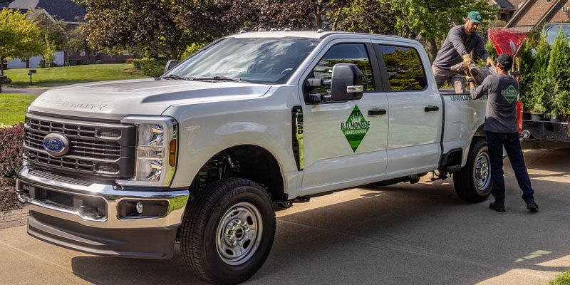 White Ford Super Duty landscaping truck with R.D. Monroe Landscaping logo, being loaded by two landscapers.