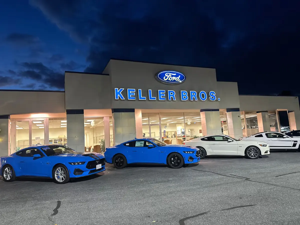 Night shot of Keller Bros. Ford Lititz dealership with Ford and Keller Bros. signs illuminated, and several Mustang cars parked out front.